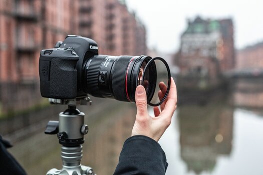 Außenaufnahme: Hand eines Fotografen setzt magnetischen F:X Pro Rundfilter auf Canon Kamera auf Stativ, seitliche Ansicht