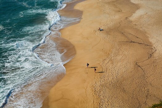 3 Personen am sonst leeren Strand, links Meer mit Wellengang - Beispiel für Drohnenfotografie
