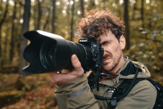 Mann fotografiert mit Nikon D810, Kamera ist mit dem SNAPSNAP camera strap von FIDLOCK am Rucksack befestigt