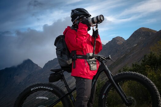 Radfahrerin steht neben ihrem Rad und fotografiert mit Kamera und Steadify