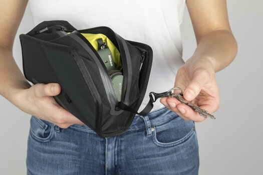 Frau hält leicht geöffnete TWIST essential bag in einer Hand, in der anderen Hand einen an der Tasche befestigten Schlüssel.