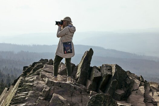 Frau steht auf Felsgestein vor Landschaftskulisse und fotografiert.