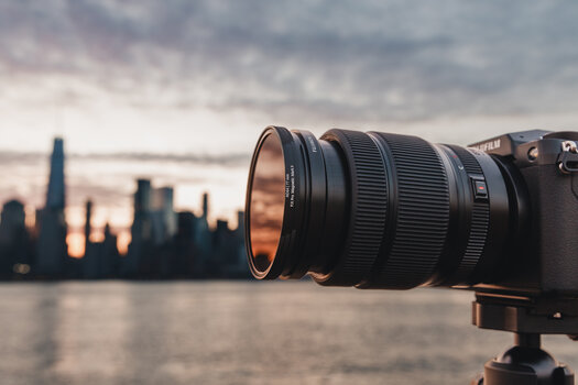 Seitenansicht: FUJIFILM-Kamera mit Objektiv und einem Filter aus dem F:X Pro ND-Filter-Set Mark II vor Skyline im Abendlicht