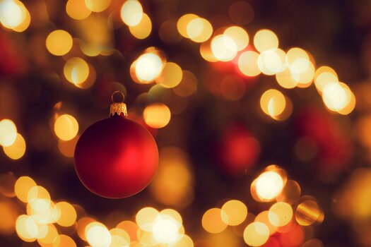rote Weihnachtskugel am Baum, im Hintergrund Bokeh der Lichterkette und unscharf weitere Kugeln