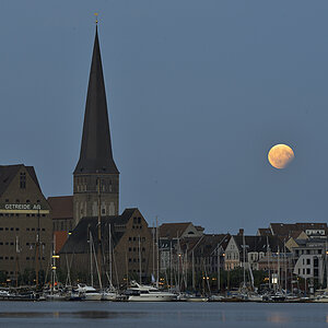Zu sehen ist die Petrikirche, etwas Hafenkulisse und der gerade aufgegangene Mond, der gerade ein wenig den Erdschatten abbekommt.