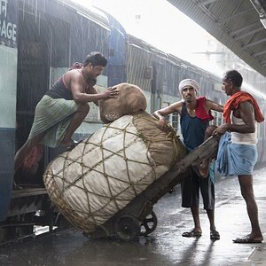 Auf einem Bahnhof in Kalkutta wird ein Gepäckwagen während eines Monsunregens entladen