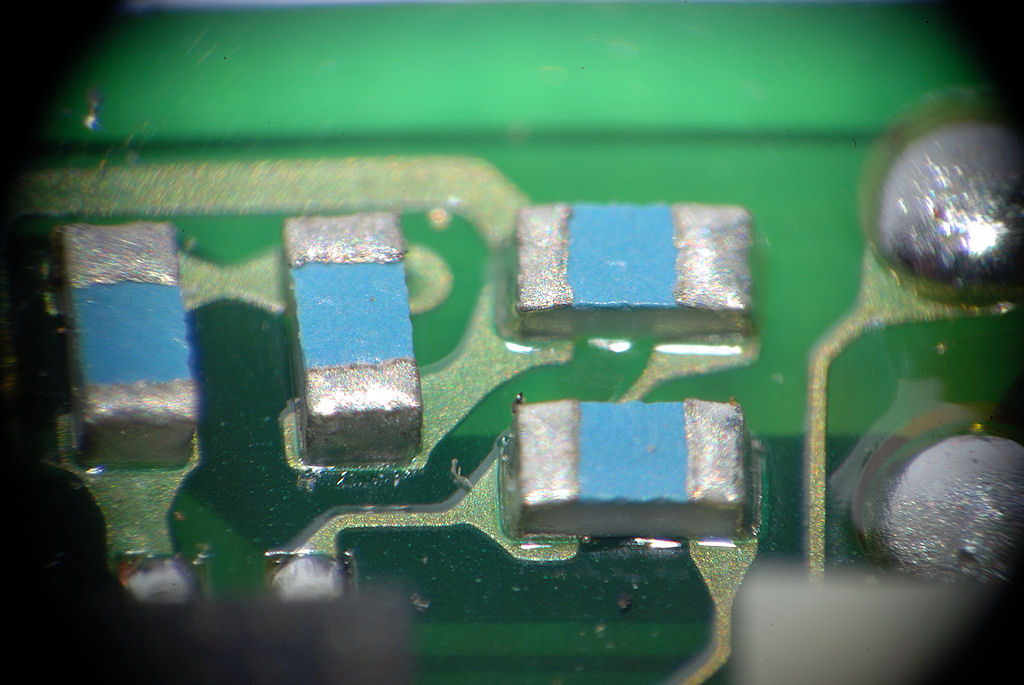 Mit selbstgebasteltem Lupenobjektiv (Maßstab 1:5,5):
Winzige SMD-Kondensatoren auf einer kleinen Nikon-AF-S-Motorplatine