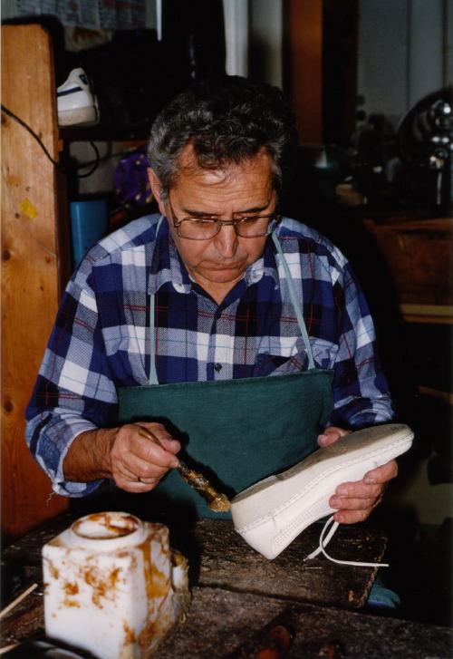 Schuhmacher beim einpinseln eines Schuhs damit ein neuer Absatz angeklebt werden kann. Ca. 1990.