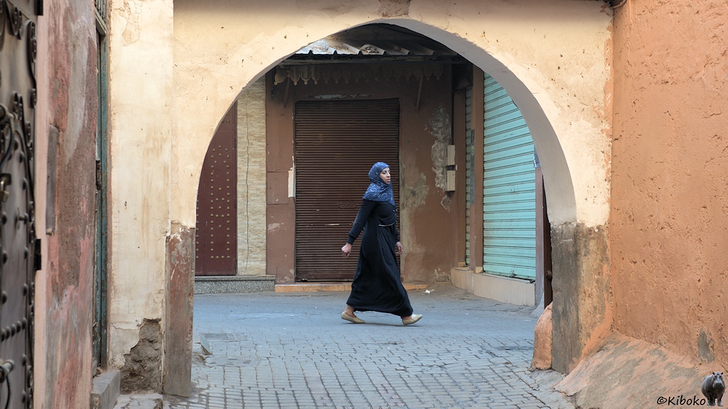 Eine Frau in schwarzer Tracht und blauem Kopftuch huscht an einem Torbogen vorbei. Die Läden im Souk sind noch geschlossen.