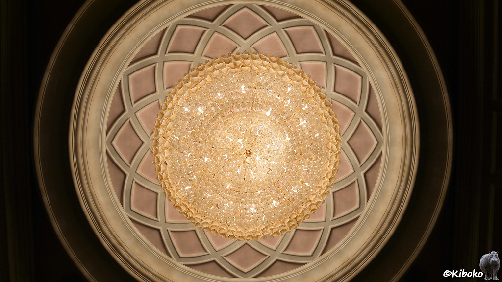 Das Bild zeigt einen Deckenleuchter von unten. Viele hundert Glaskugeln. Darum sind ornamente in die Decke eingebracht.