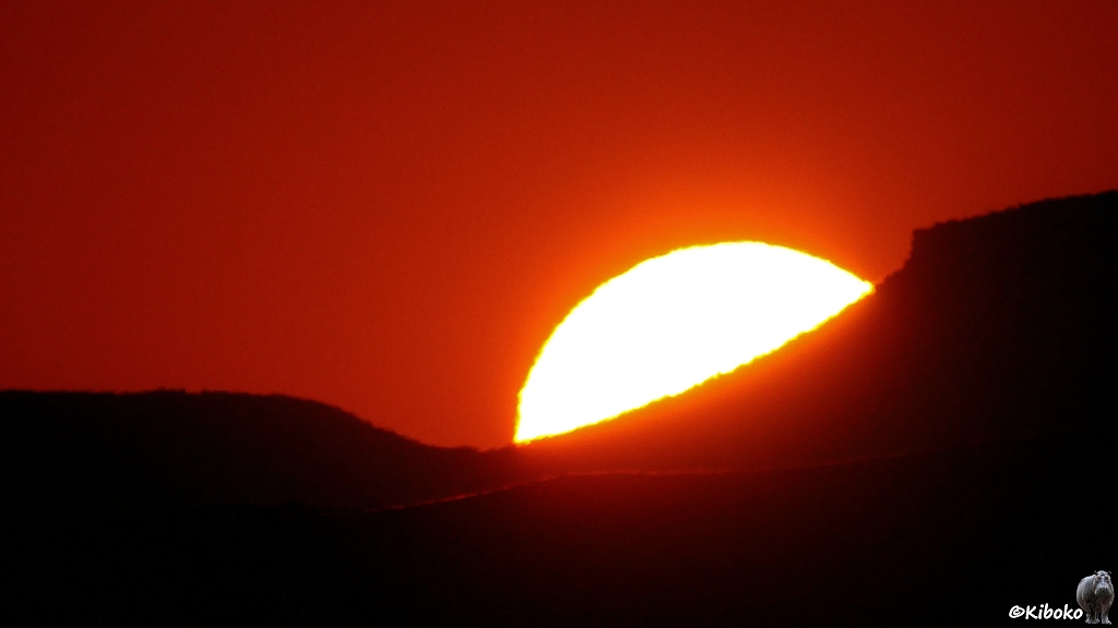 Die Sonne geht hinter einem Berghang auf. Der Himmel leuchtet rot.