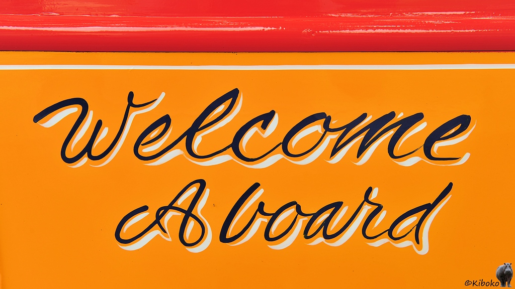 Das Bild zeigt eine Aufschrift in schwarzer Schreibschrift mit weißem Schatten auf gelben Grund: Welcome Aboard.