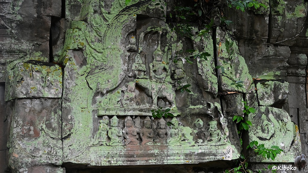 Das Bild zeigt ein mit hellgrünen Flechten überzogenes Relief. Unten ist eine Reihe kleiner Firguren graviert. In der Mitte reitet der Totengott Yama einen Büffel. Blätter umranken das Relief.