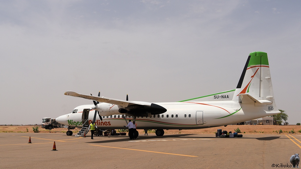 Das Bild zeigt eine weiße, zweimotorige Propellermaschine schräg von Hinten auf einem Flugfeld. Die Maschine hat orange und grüne Zierlinien und die Aufschrift Niger Airlines.