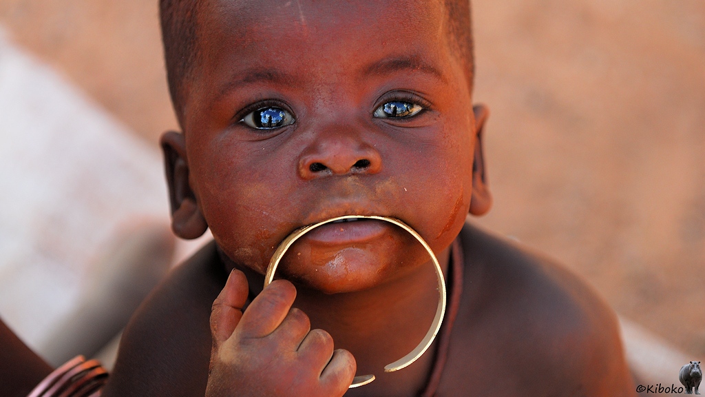 Porträt eines kleinen Jungen, der einen Messingring mit Mund und Hand hält. In den Augen spiegelt sich der blaue Himmel.
