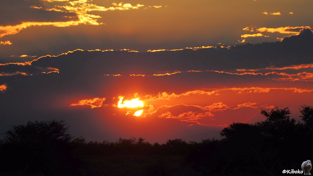 Die Sonne versinkt zwischen mehreren Wolken. Die Wolkenränder leuchten durch die Sonne.