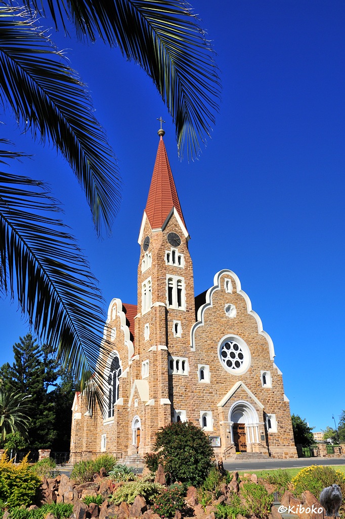 Bild im Hochformat mit einer Kirche aus hellbraunen Natursteinen und weißen Verzierrungen.