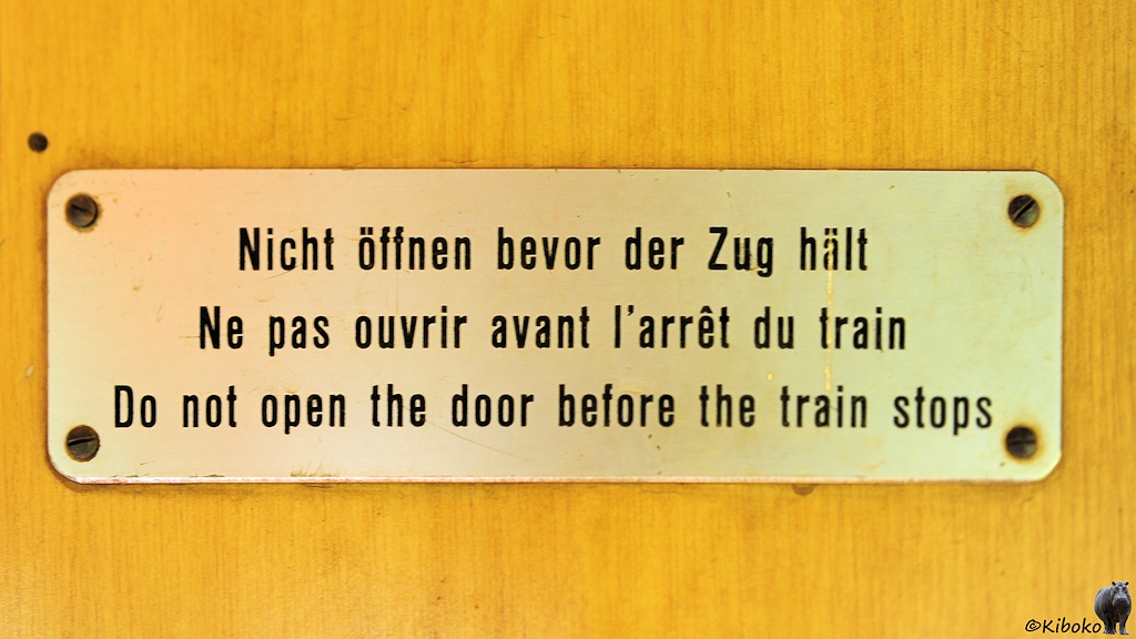 Das Bild zeigt ein angeschraubtes Schild an der Wand im Eingangsbereich des Wagens.