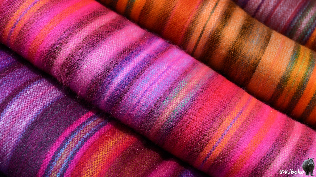 Das Bild zeigt vier Stoffe mit schmalen Streifen in den Farben von violett, rosa bis orange. Das Bild ist schräg gestellt, so dass der Stapel nach diagonal durch das Bild läuft.