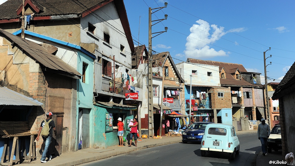 Straßenszene in Antananarivo. Hochspannungsmasten stehen in den engen Straßen und führen an Geschäften und Balkonen vorbei.