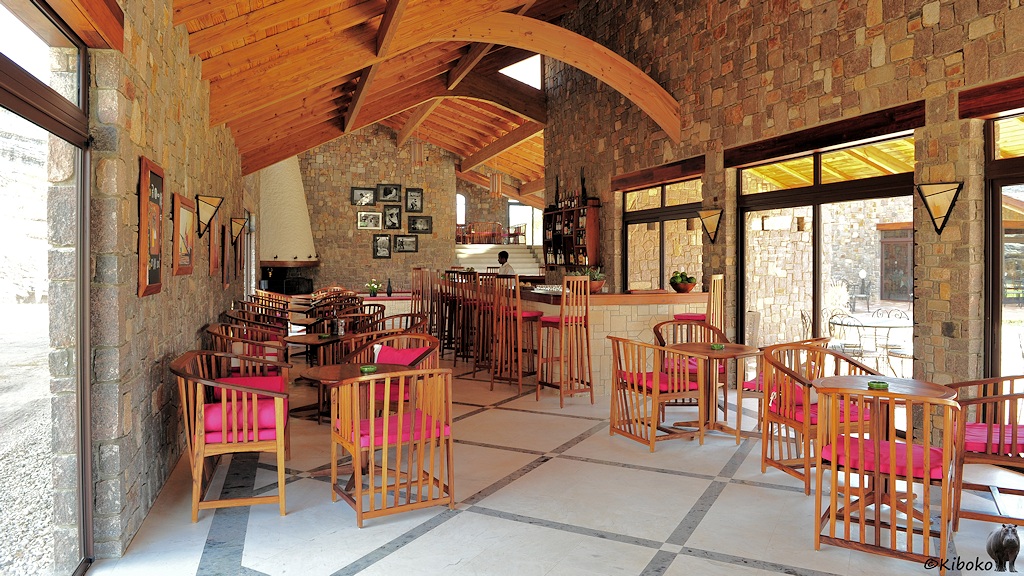 Das Bild zeigt einen Innenraum mit Natursteinwänden. Rechts ist eine Bar mit Theke und Barhockern. Rechts sind kleine Tische, sowie Holzstühle mit roten Sitzkissen.