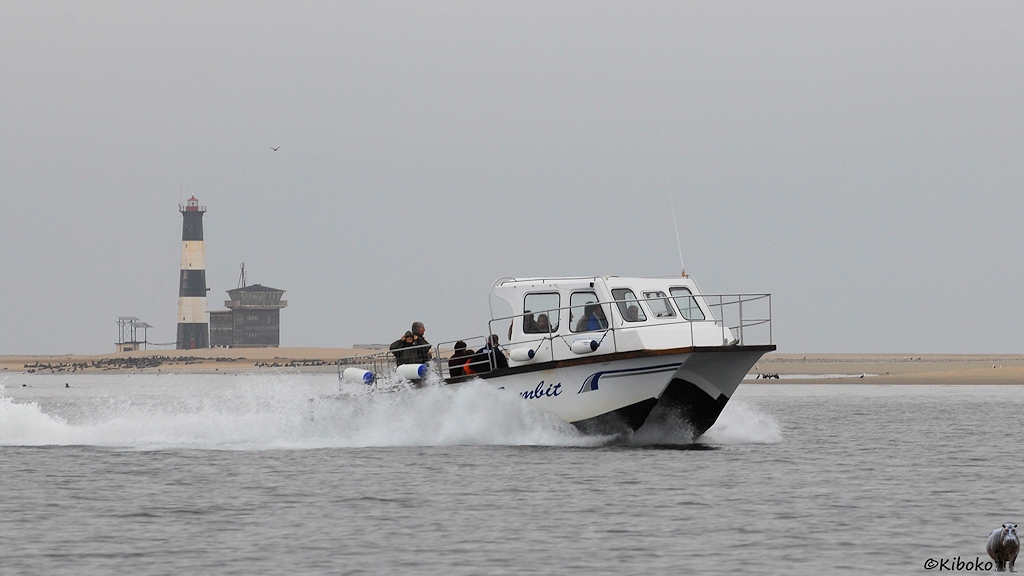 Ein kleines, weißes Boot mit Dopopelrumpf fährt mit hoher Geschwindigkeit an einen schwarz-weiß geringelten Leuchtturm vorbei.