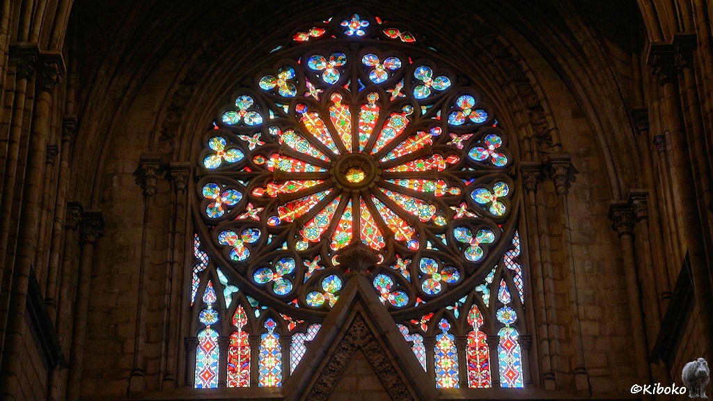 Das Bild zeigt die bunten Glasfenster einer Rosette über dem Eingang.