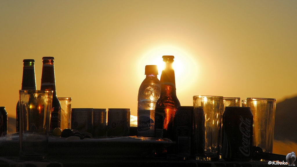 Getränkeflaschen und Gläser mit der untergehenden Sonne im Hintergrund.