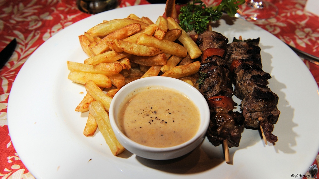 Zwei Fleischspieße mit Pommes und einen Napf mit hellbrauner Soße.