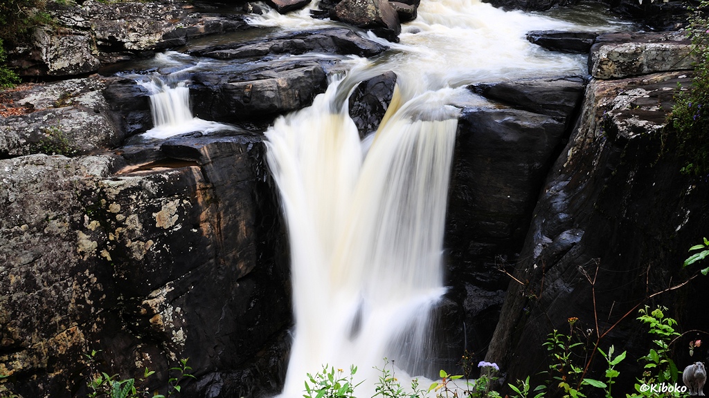 Das Bild zeigt einen kleinen Wasserfall zwischen grauen Felsen. Die Belichtungszeit ist etwas länger. Das Wasser scheint zu fließen.